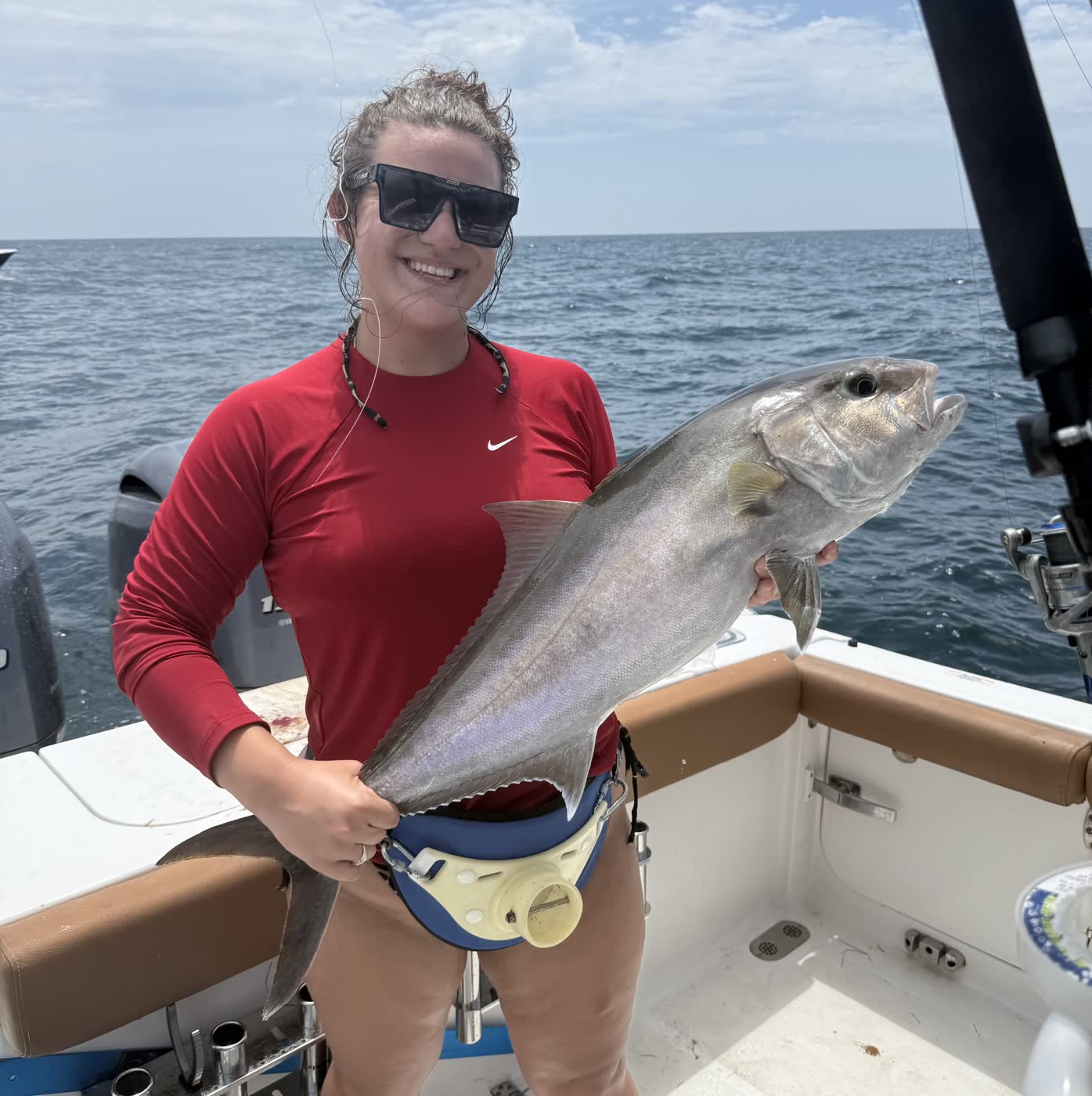 A customer showing off a big amberjack catch with the beautiful Gulf waters behind her
