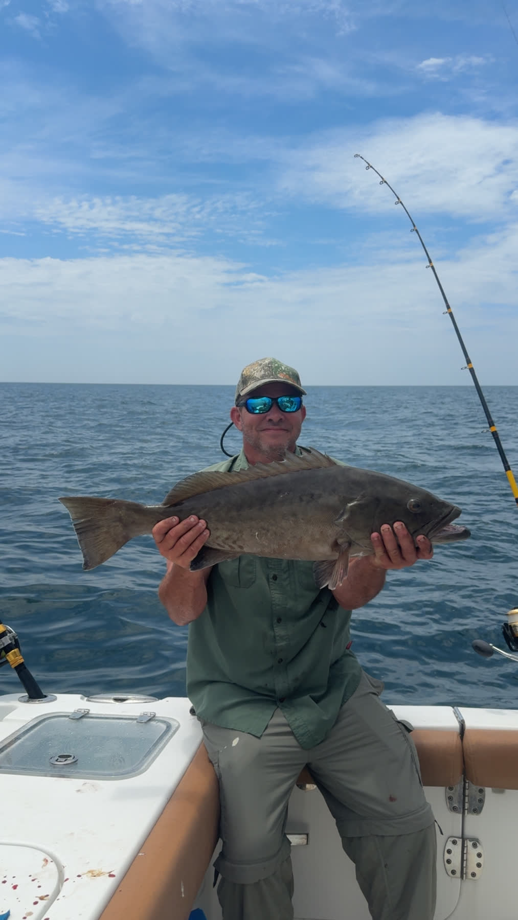 A customer proudly holding up a big grouper catch aboard the boat